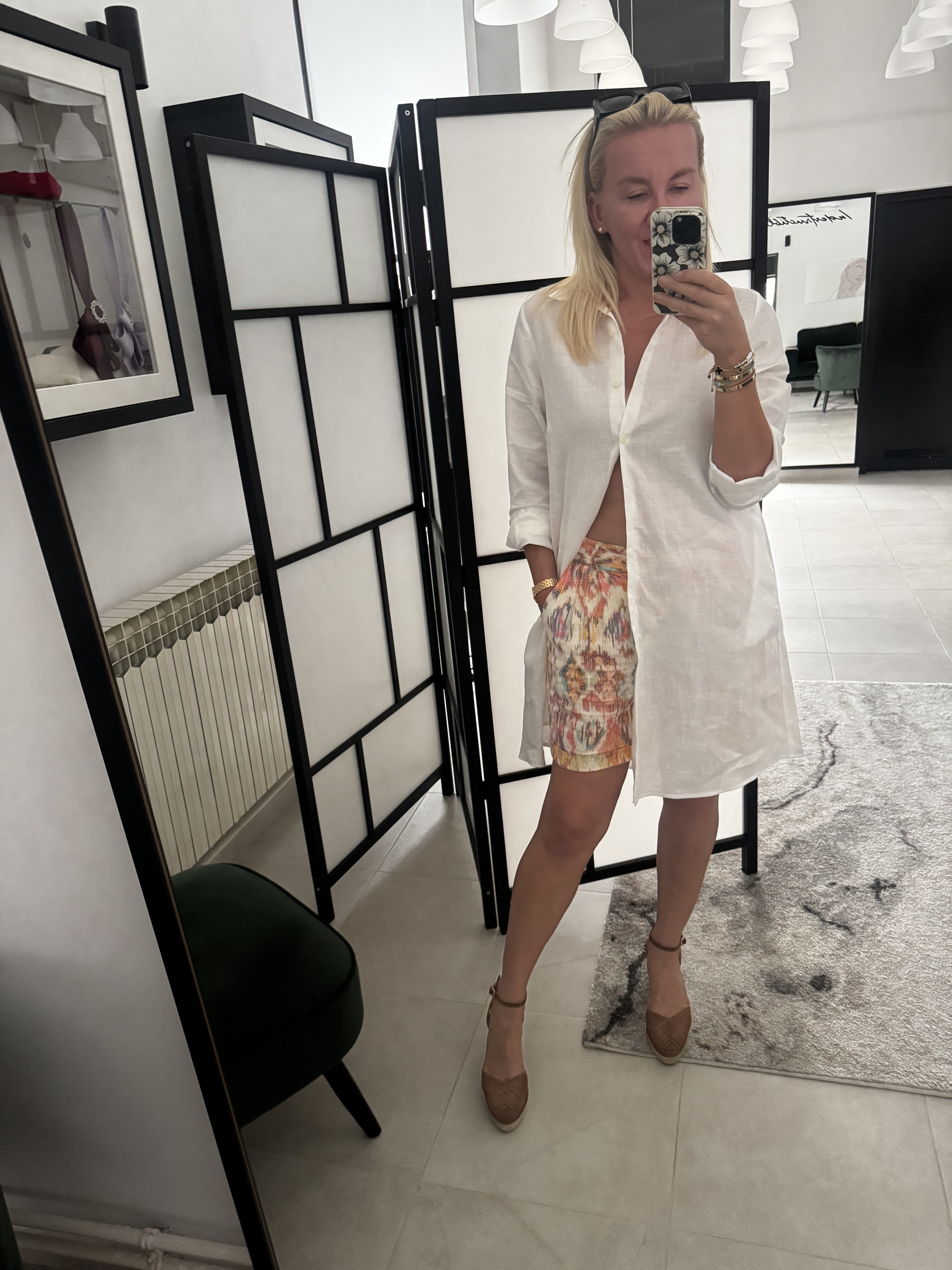 Žena nosi bijelu lanenu košulju dužeg kroja preko šarenih kraktih hlačica